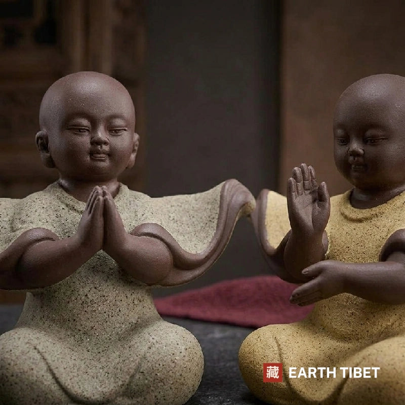 Close view of two baby monk statues, one with palms together and one with a hand raised