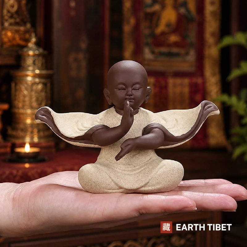 Seated baby monk figure with wide sweeping sleeves on a dark surface