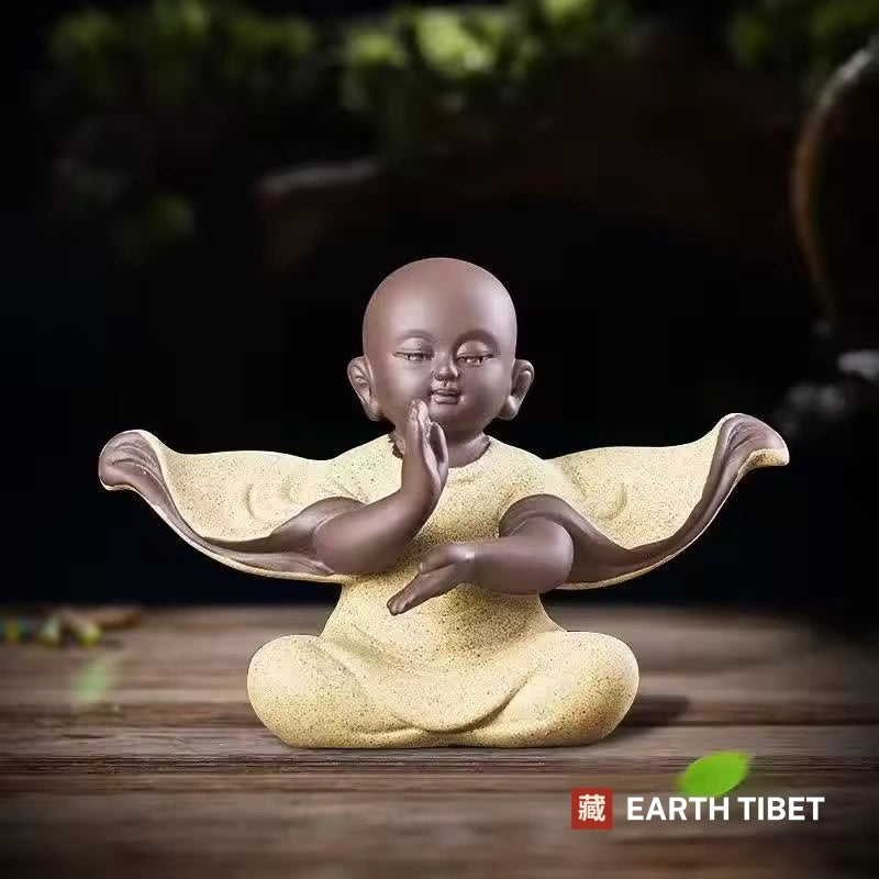 Yellow baby monk statue with one hand raised and one extended, sleeves spread wide
