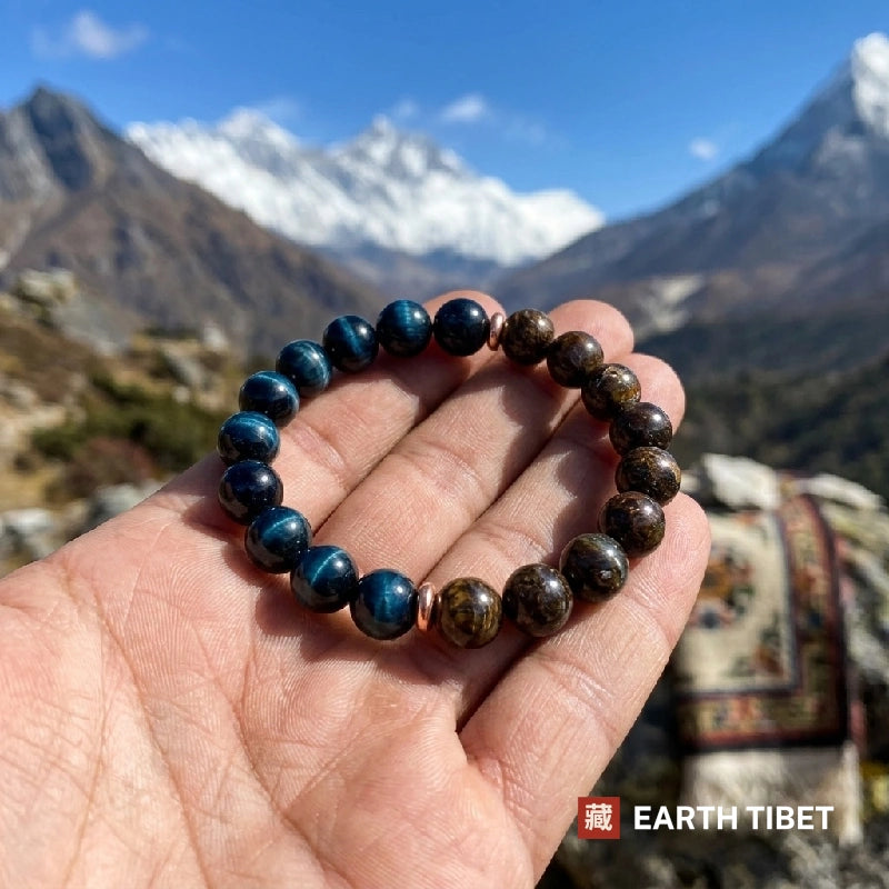 Blue tiger eye and bronzite bracelet held in a palm against Himalayan mountains