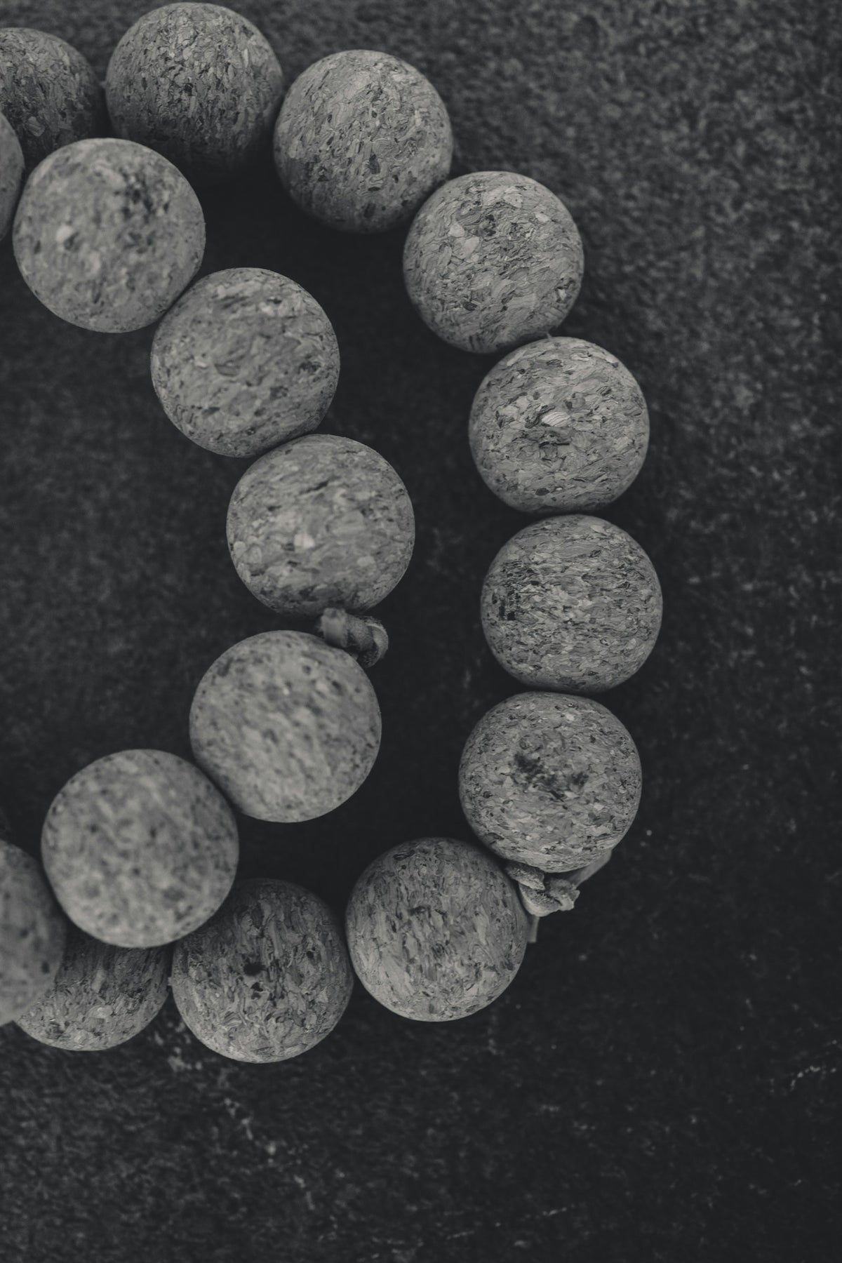 A strand of grey natural stone beads on a dark surface, each bead pitted and mottled