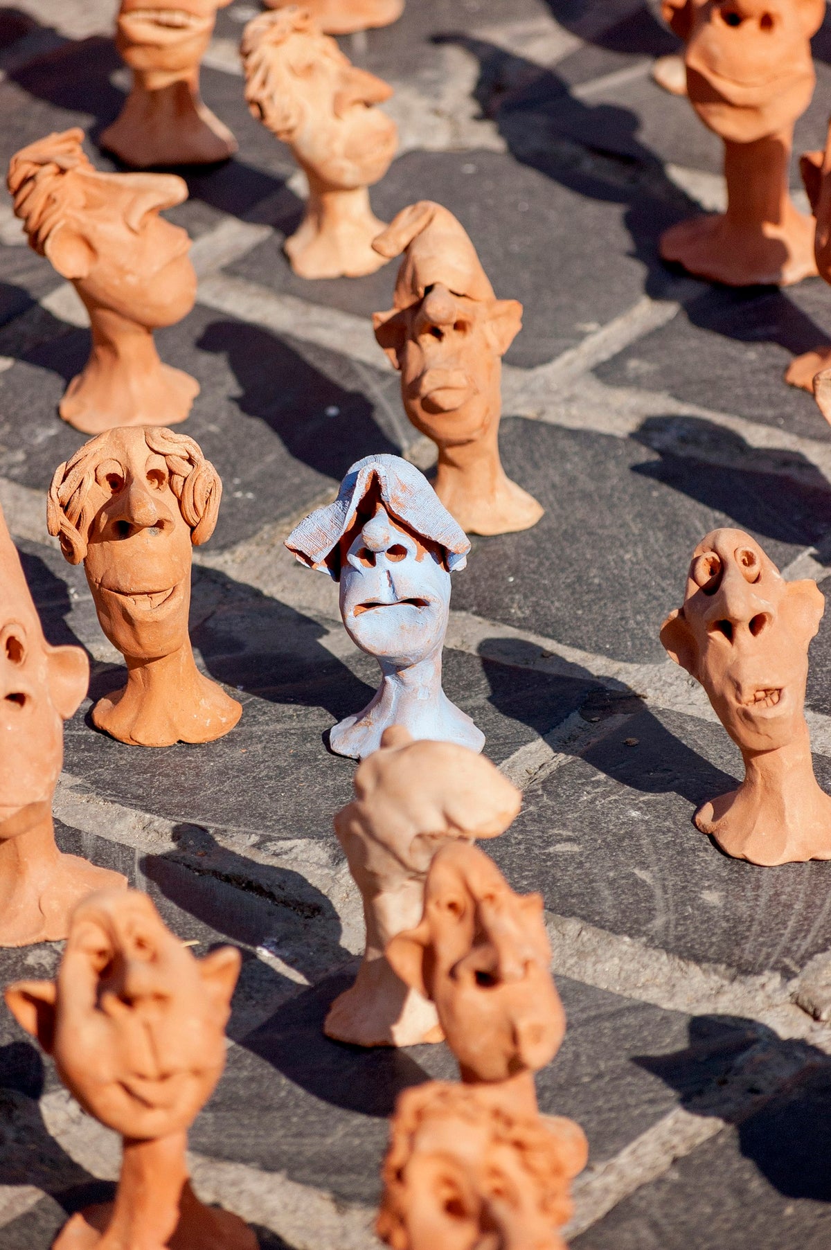Rows of hand-sculpted clay heads drying in a workshop, every face slightly different