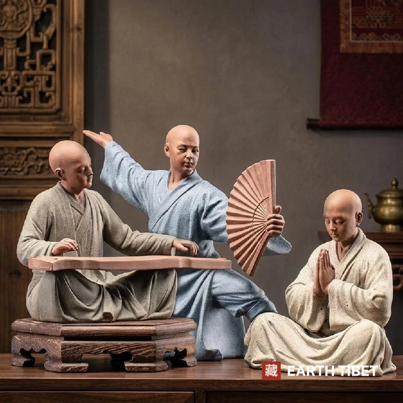 Three Chinese scholar monk statues in ceramic: one playing a guqin, one standing with a fan, one with palms together