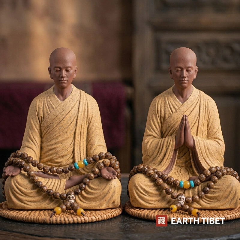Two ceramic meditating monk statues, one with palms together and one with hands in the lap