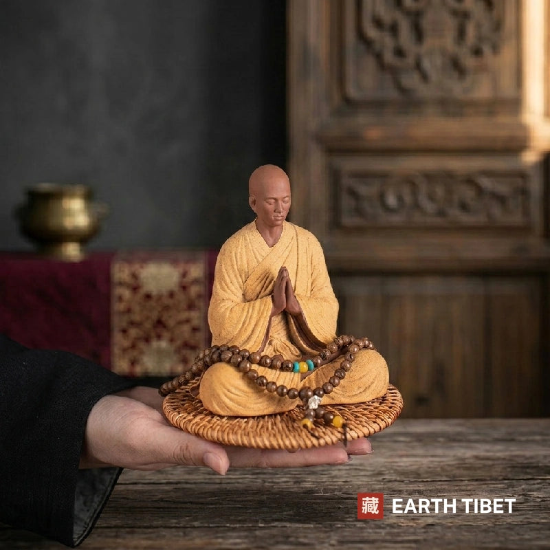 Ceramic monk statue seated in meditation on a woven rattan mat