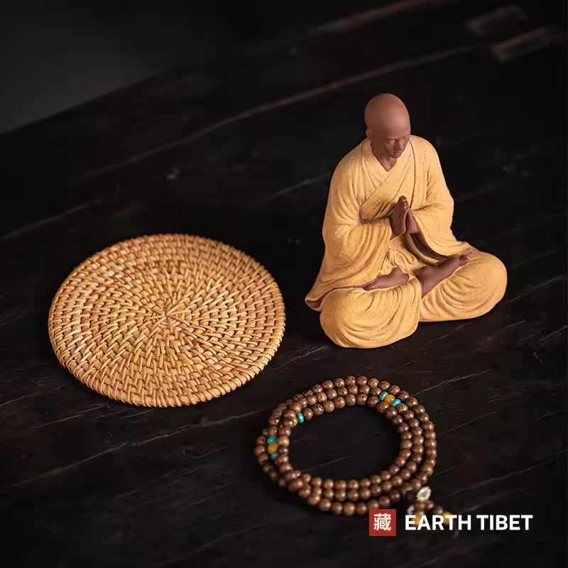 What is included: ceramic monk with palms together, woven rattan mat and a mala