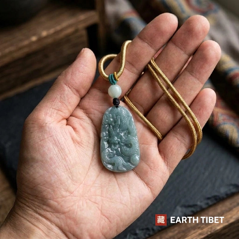 Carved jade dragon plaque and its gold-toned cord lying in an open hand