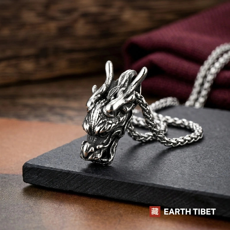Chinese dragon head pendant lying on slate beside its steel wheat chain