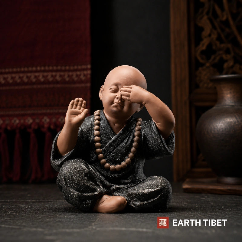 Ceramic monk figure covering his eyes, see no evil, seated on dark slate