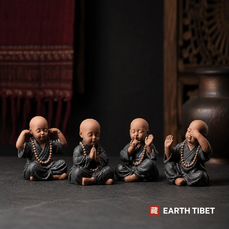 Four ceramic monks arranged on dark slate below a red Tibetan textile and a brass vessel