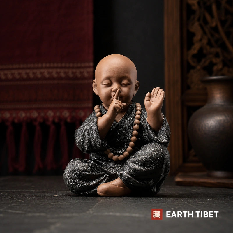 Ceramic monk figure covering his mouth, speak no evil, in a dark glazed robe