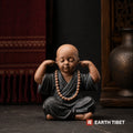 Ceramic monk figure covering his ears, hear no evil, with mala beads over his robe