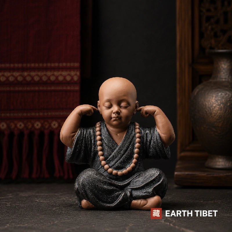Ceramic monk figure covering his ears, hear no evil, with mala beads over his robe