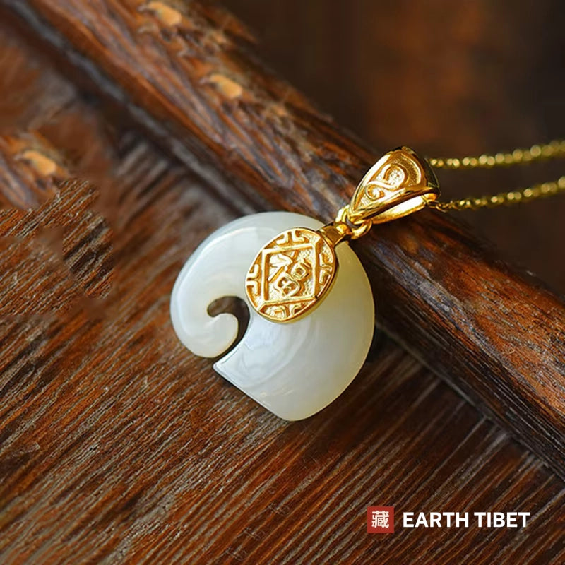 White jade elephant pendant with a gold fu plaque, on a wooden surface