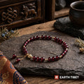 Chinese garnet vitality bracelet on dark slate beside a carved Tibetan chest