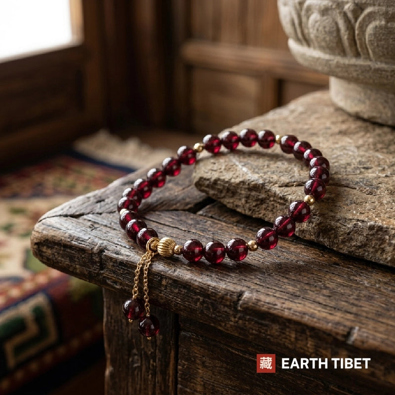 Garnet bracelet resting on a weathered wooden ledge with the gold chain drop hanging