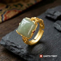Square green chalcedony cabochon in a gold-toned scrollwork band on slate