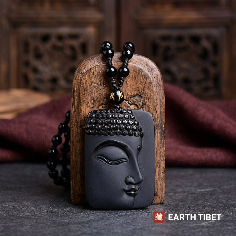 Black obsidian Buddha face pendant on a beaded cord against carved wood