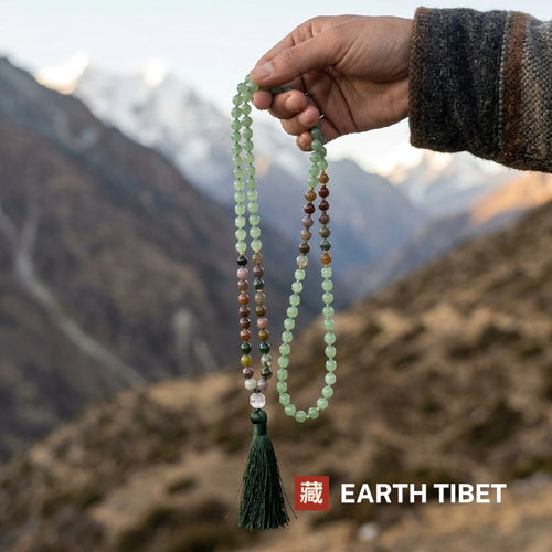Green aventurine and Indian agate mala held up against a Himalayan valley