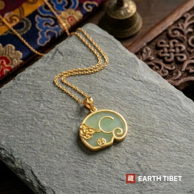 Green jade elephant pendant and its gold-toned chain laid on slate
