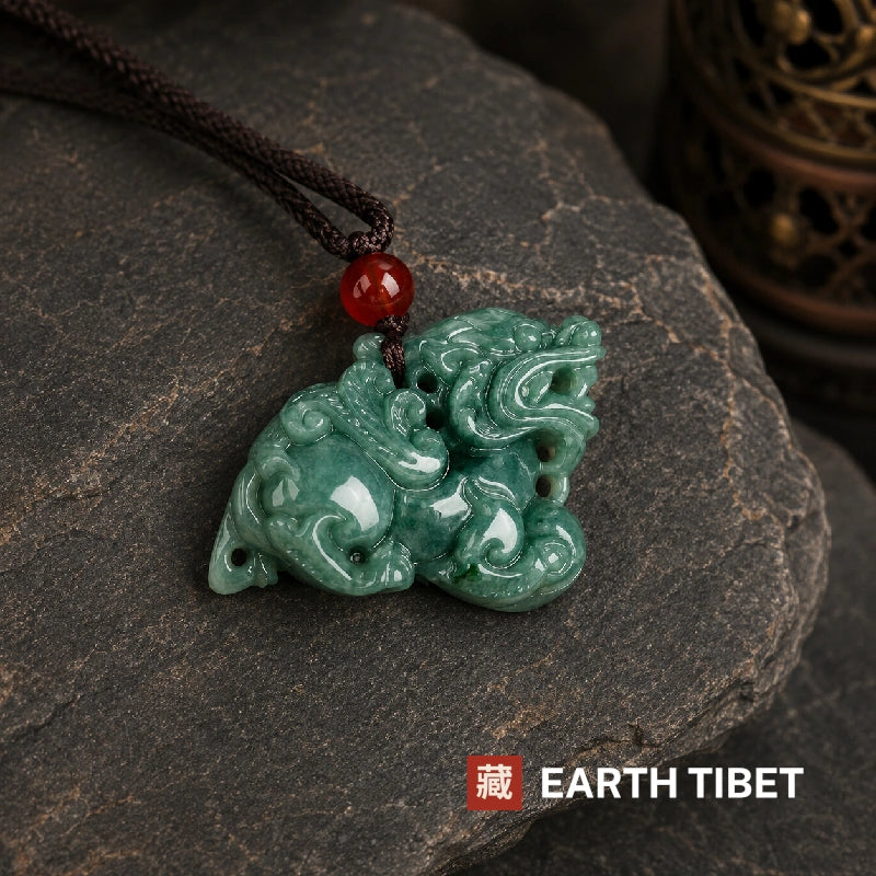 Jadeite pixiu pendant lying on dark stone with its braided cord