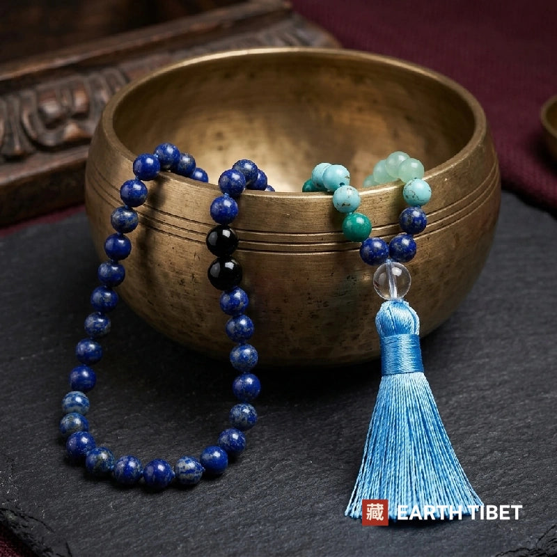 Lapis lazuli mala beside a brass singing bowl, the two black onyx marker beads visible
