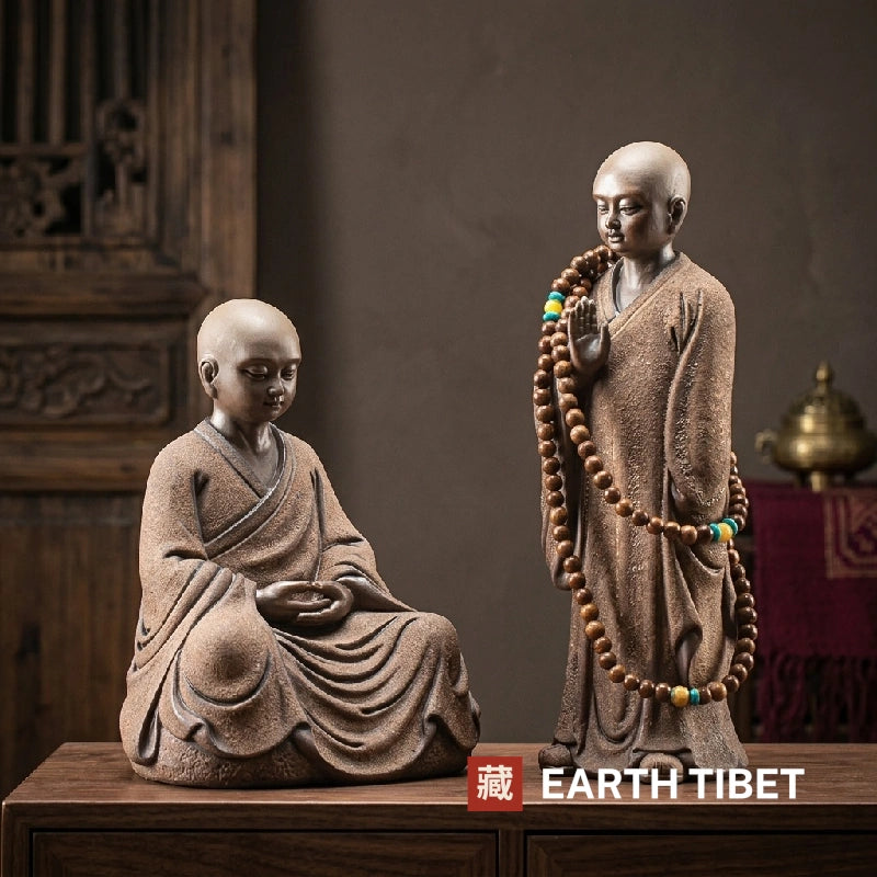 Seated and standing little monk statues side by side on a wooden cabinet