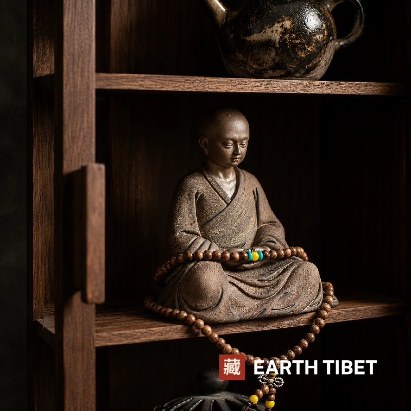 Seated little monk statue on a wooden shelf beneath a teapot