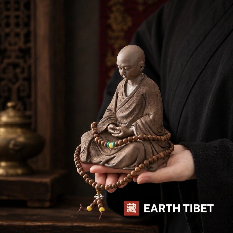 Seated little monk statue held on an open hand for scale