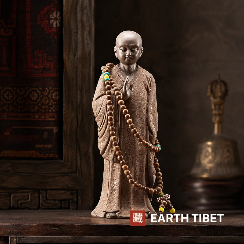 Standing little monk statue from the front, one palm raised before the chest