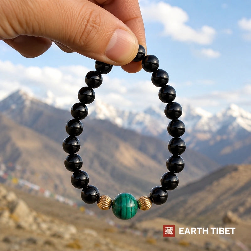 Black tourmaline and malachite bracelet held against snow-capped mountains and prayer flags