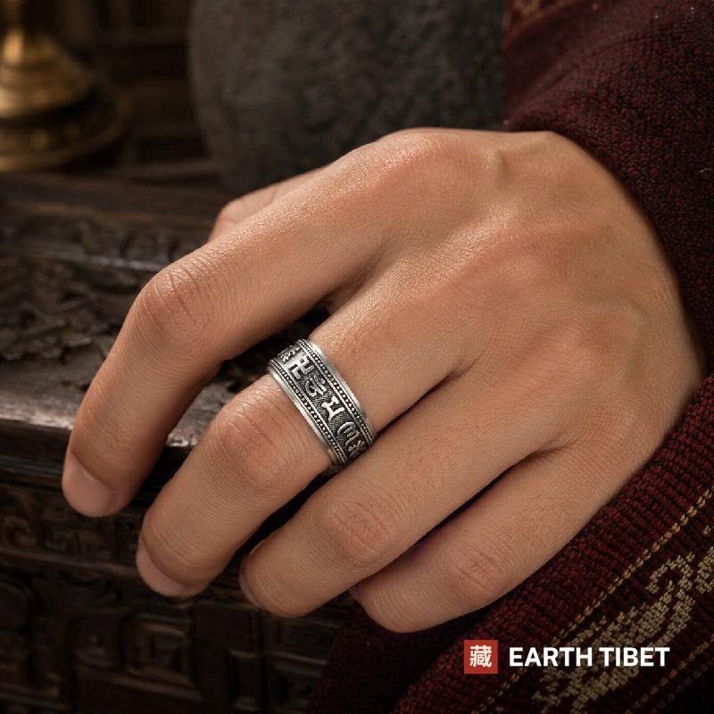 Man wearing the om mani padme hum spinner ring, with a dark maroon sleeve and carved wood behind