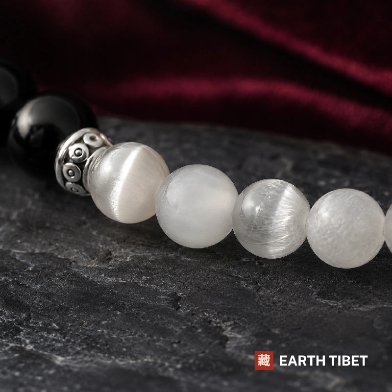 Close up of fibrous white selenite beads beside polished black onyx and a carved silver-toned barrel