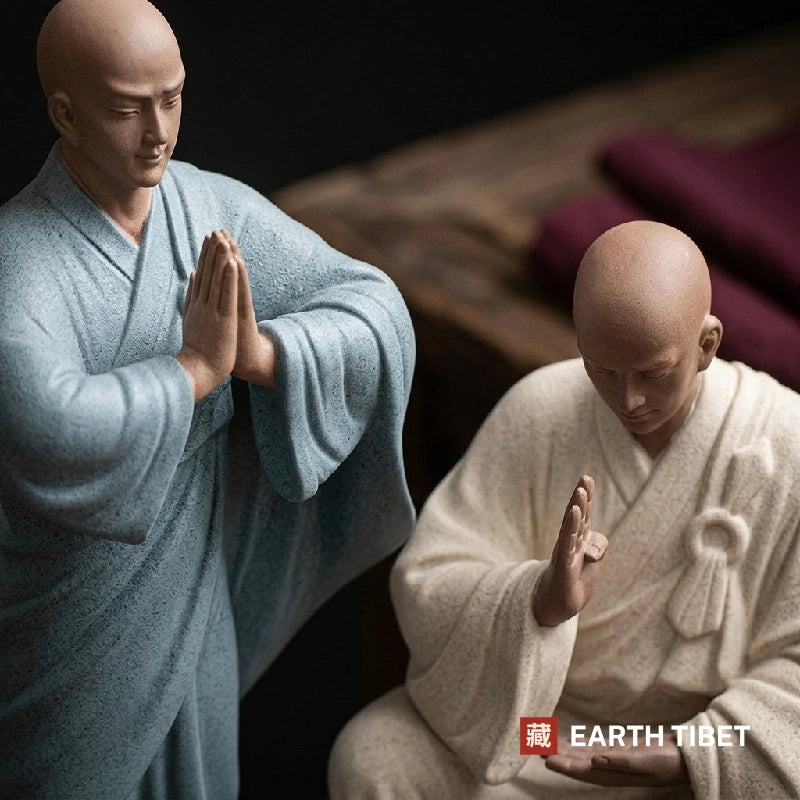 Purple clay monk statue seated in a cream robe with one palm raised