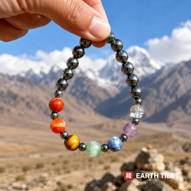Chakra bracelet held against snow peaks with a mani stone cairn behind