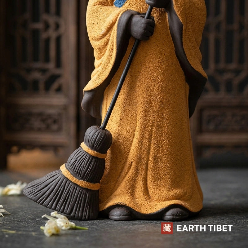 Close view of the clay broom, its bound rings and individual bristles, beside bare feet under the hem