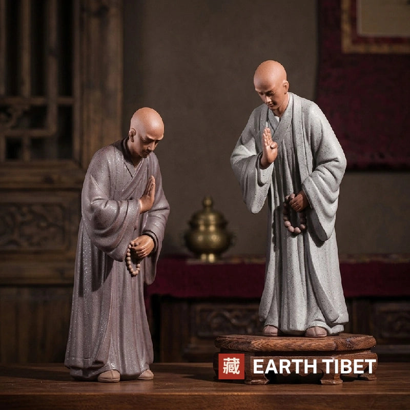 Two tall ceramic zen monk statues, one bowing and one with a hand raised in blessing