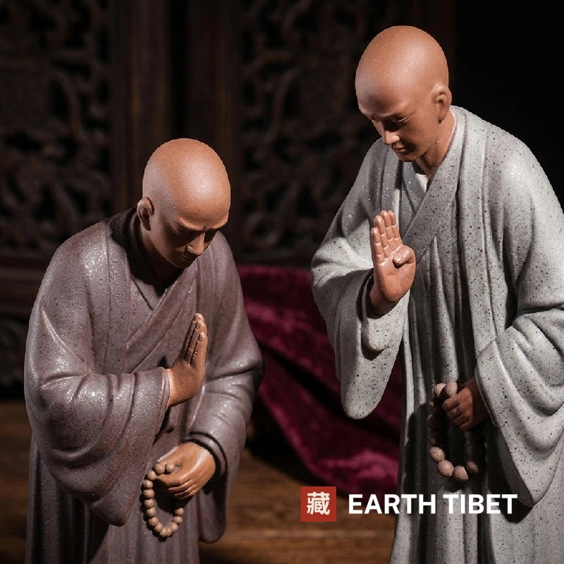 Close view of two ceramic monk statues showing the raised hand and the pressed palms