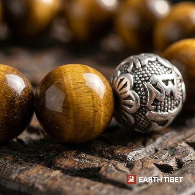 Close view of a silver bead cast with Tibetan mantra script beside a tiger eye bead