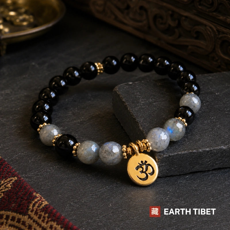 Faceted labradorite beads flashing blue beside black tourmaline, with an om charm