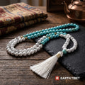 Turquoise and howlite 108 bead mala coiled on a wooden table with a copper kettle behind