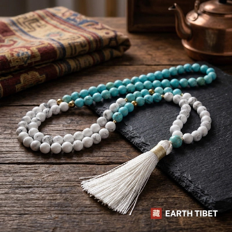 Turquoise and howlite 108 bead mala coiled on a wooden table with a copper kettle behind