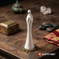Matte white ceramic zen figure on a wooden table beside a brass box and river stones