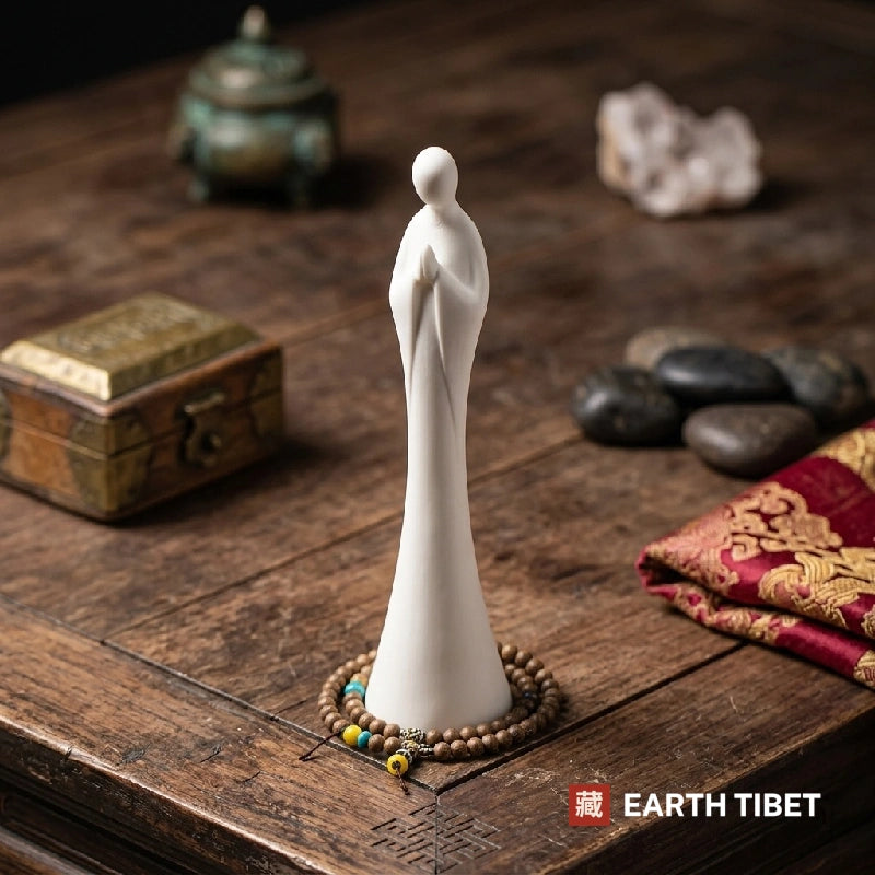 Matte white ceramic zen figure on a wooden table beside a brass box and river stones