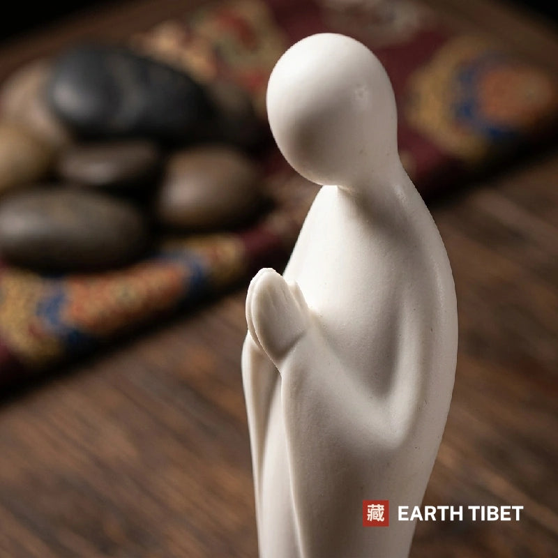 Close view of the bowed head and joined palms on the white ceramic zen figure