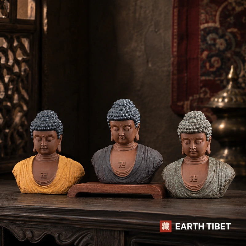 Three Buddha head statues in ochre, slate blue and pale green-grey on a dark wood table