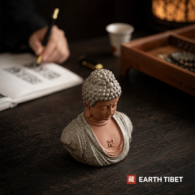 Shakyamuni Buddha head statue on a wooden stand beside a tea set