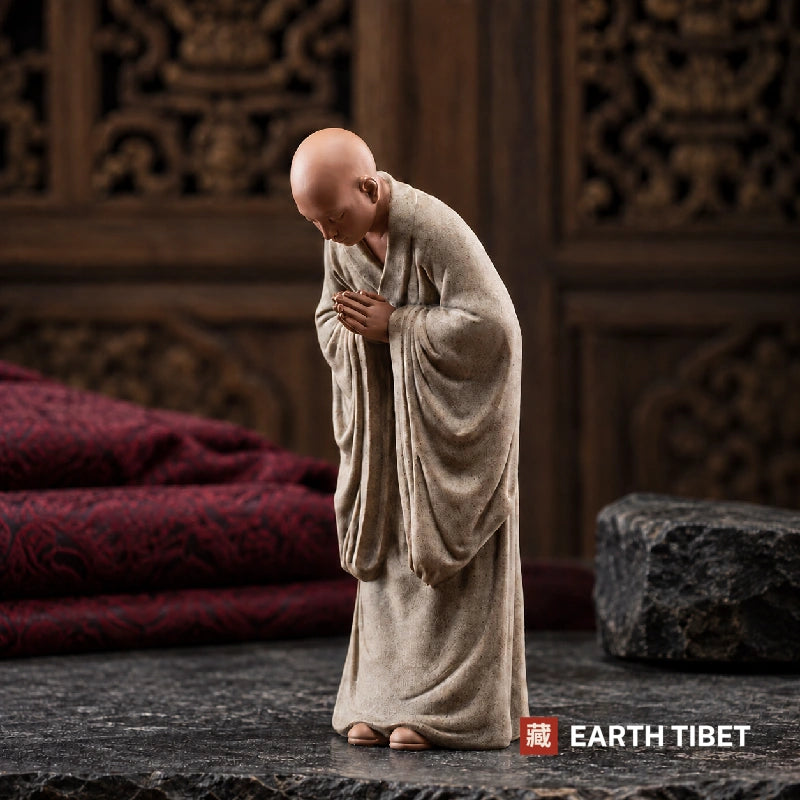 Grey bowing monk statue alone, head lowered, bare toes showing below the hem