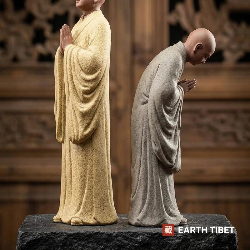 Side view of the standing and bowing monk statues showing the matte sandy clay surface