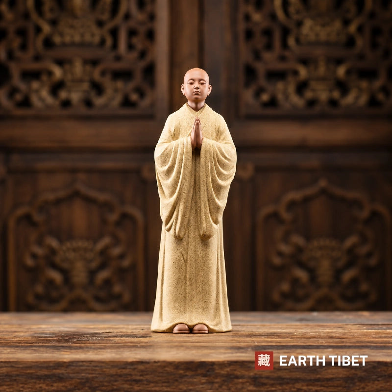 Front view of the beige standing monk statue, palms joined at the chest, bare feet below the robe